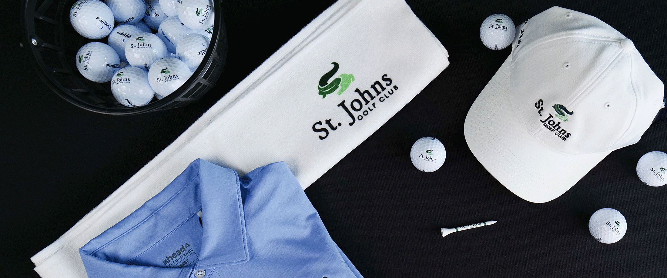 SJGC gear, including golf balls, hats, a shirt, and a towel, lay against a black background.,