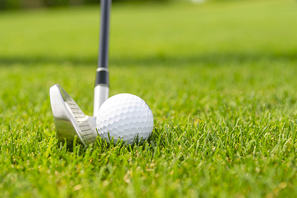 A golf ball about to be hit by a golf club on green grass